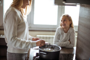 Young girl cooking food with adult in the kitchen.