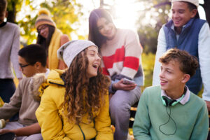 Happy teenage boy and girl laughing while sitting with their friends.