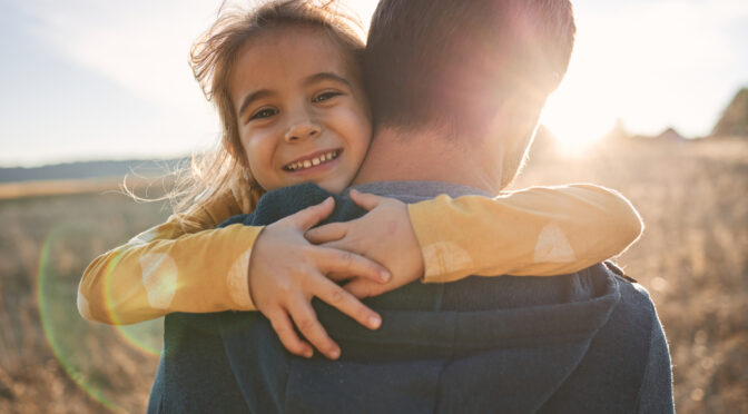 Young girl outside hugging father.